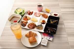 Una mesa con diversos alimentos, entre ellos un plato de cruasanes, un vaso de zumo de naranja y varios recipientes pequeños con diferentes comidas y condimentos.
