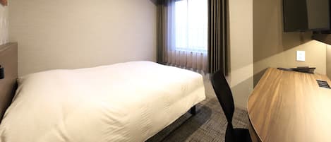 A hotel room with a bed, a desk, a chair, a television, and a window with curtains.