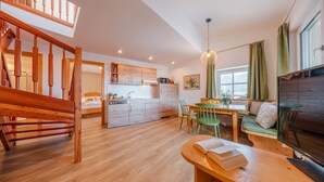 A modern kitchen with wooden cabinets, a dining area with a green chair, and a wooden bench with a book. - Maisonette with Timeless Elegance & Panoramic Views (Nals Südtirol)