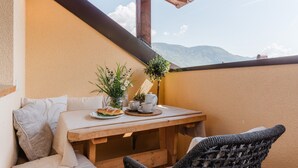 A wooden table with a white tablecloth, a vase with flowers, a teapot, and a plate with food. There are wicker chairs and a cushioned bench. - Maisonette with Timeless Elegance & Panoramic Views (Nals Südtirol)