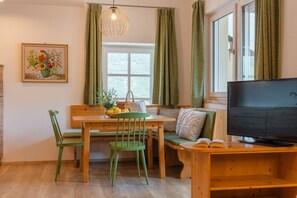 A room with a wooden dining table, green chairs, a TV, and a window with curtains.