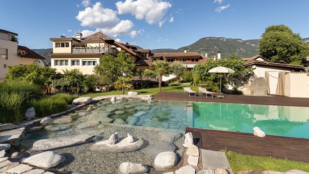A pool area with a clear view of the mountains, a wooden deck, and a stone pathway leading to the pool. - Maisonette with Timeless Elegance & Panoramic Views (Nals Südtirol)