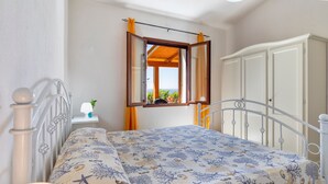 Un dormitorio con una cama, una ventana con cortinas, un armario y una pequeña mesa con una planta.