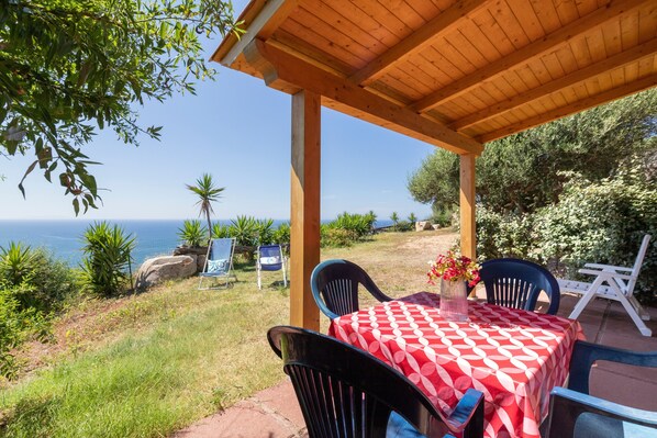 Eine überdachte Terrasse mit Tisch und Stühlen, mit Blick auf die malerische Küste.