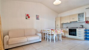 Una sala de estar con sofá y una mesa de comedor con sillas. Se observa un área de cocina con armarios y estufa.