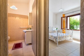 Ein Schlafzimmer mit Bett, Fenster und einem Badezimmer mit Toilette und Waschbecken.