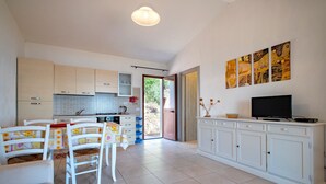 Una cocina moderna con armarios blancos, un comedor con mesa y sillas, y un televisor sobre un mueble.