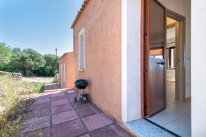 Eine Terrasse mit Grill, eine Tür zu einem Innenbereich und eine Steinmauer.
