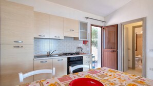 Una cocina compacta con armarios de madera clara, salpicadero de azulejos, estufa y una mesa de comedor con un plato rojo.