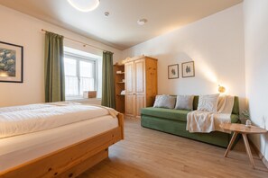 A bedroom with a bed, a green sofa, a wooden wardrobe, and a small table.