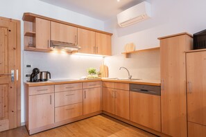 A modern kitchen with wooden cabinets, a built-in oven, a dishwasher, and a countertop with a kettle and a plant.
