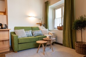 A green sofa with cushions, a small wooden table with a candle, and a plant in a basket.