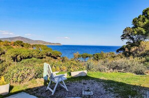Un área al aire libre con un banco y caballete, vista al mar y montañas al fondo.