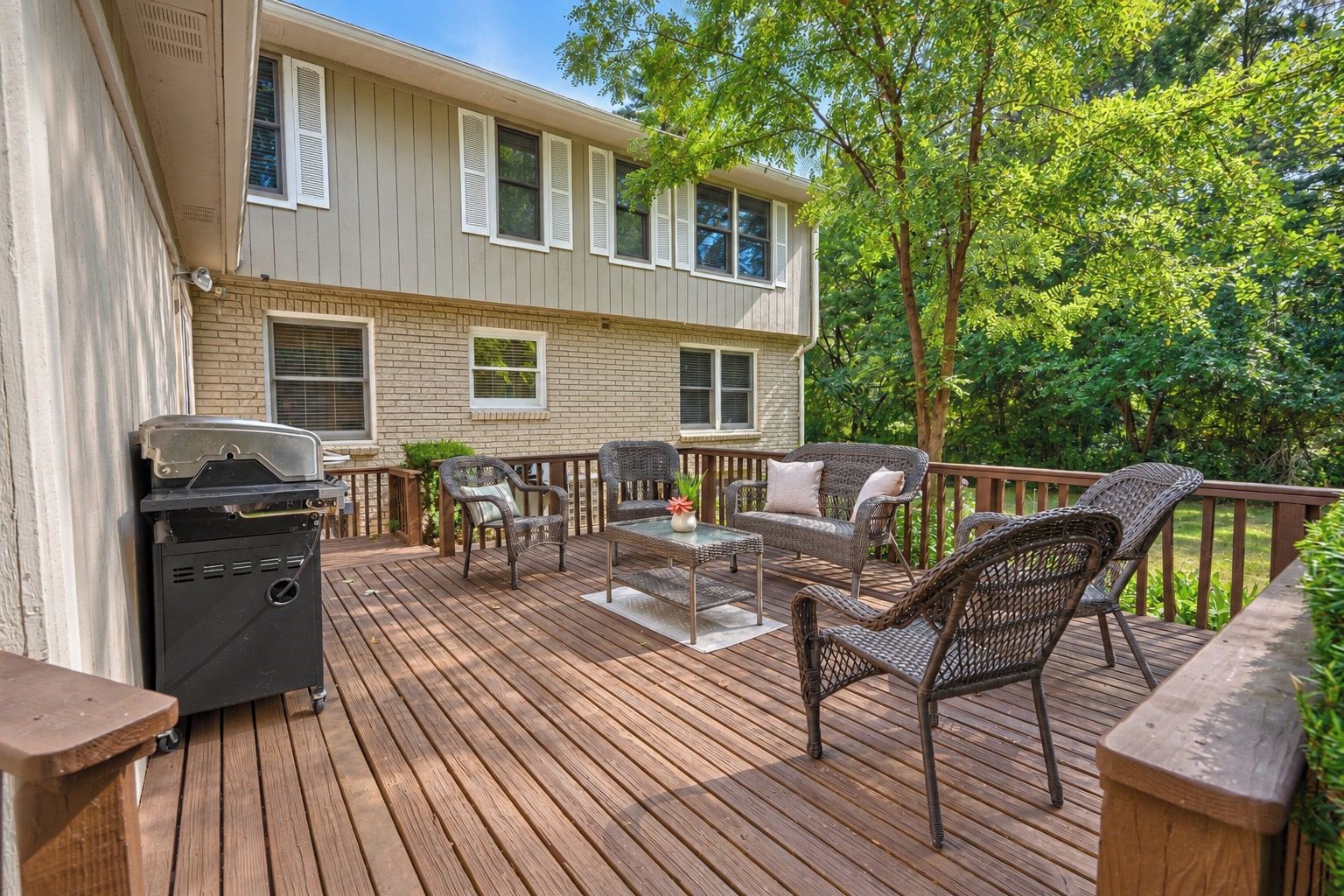 A deck with outdoor furniture, a grill, and a house in the background.