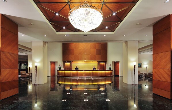 Een hotel receptie met een gepolijste marmeren vloer, een grote kroonluchter en houten lambrisering.