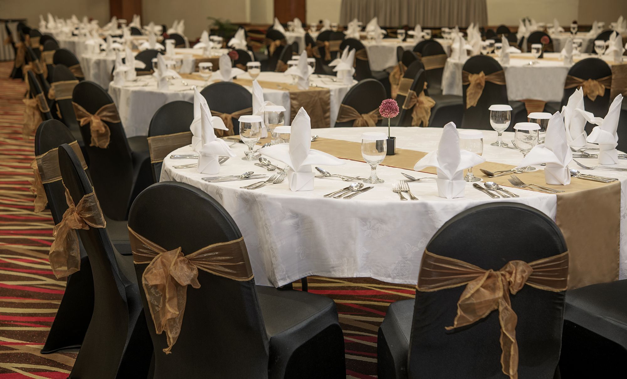 A banquet hall with round tables set for dining, each with white tablecloths, silverware, and napkins.