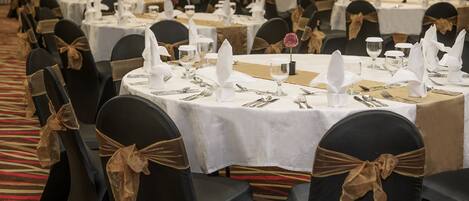 A banquet hall with round tables set for dining, each with white tablecloths, silverware, and napkins.