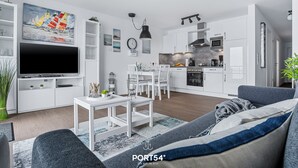 A modern living room with a TV, sofa, and dining area. - Hafenmelodie - waterfront, 1st floor, harbor view, balcony, shower room (Olpenitz)