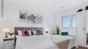 A modern bedroom with a large bed, two side tables, a window, and artwork on the wall. - Hafenmelodie - waterfront, 1st floor, harbor view, balcony, shower room (Olpenitz)