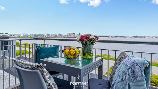 A balcony with a table, chairs, and a view of a river. - Hafenmelodie - waterfront, 1st floor, harbor view, balcony, shower room (Olpenitz)