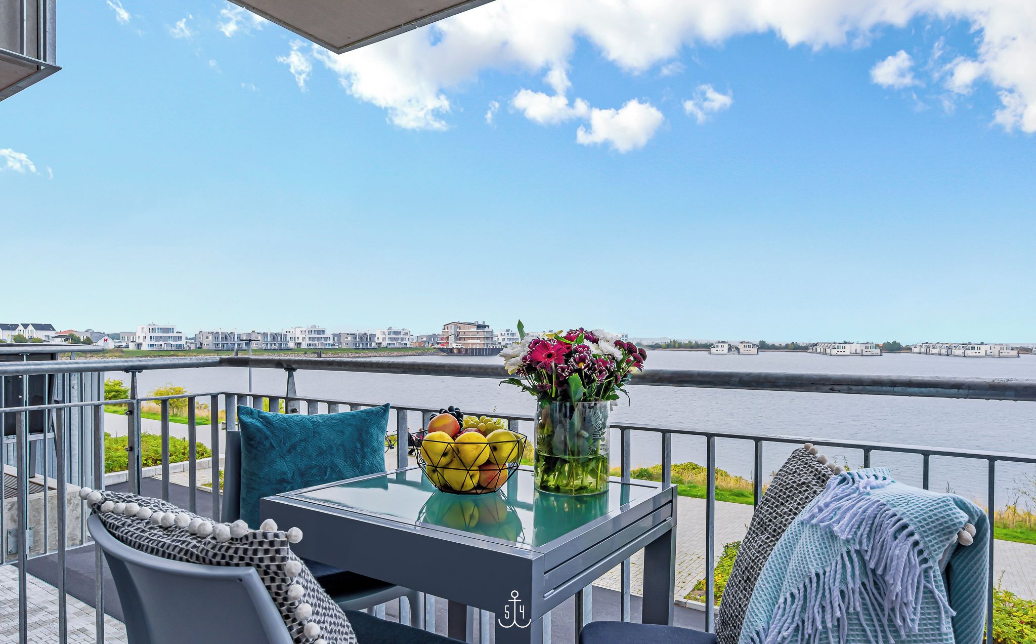 A balcony with a table, chairs, and a view of a river.
