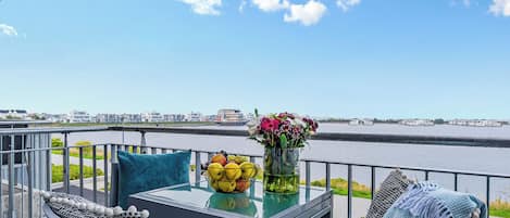 A balcony with a table, chairs, and a view of a river.
