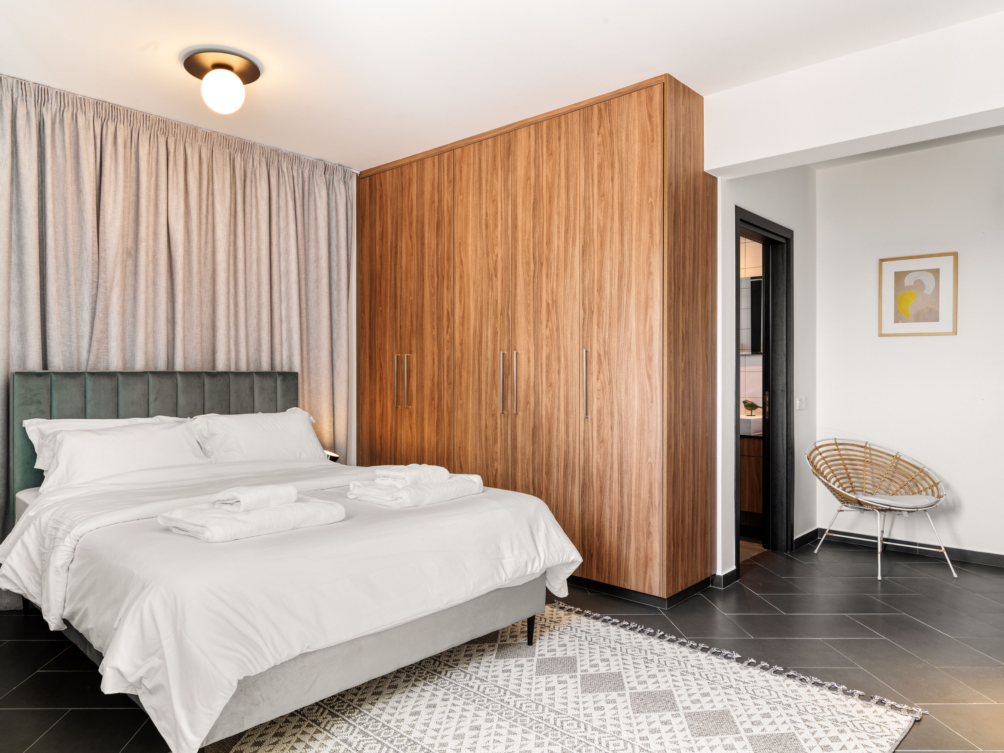 A modern bedroom with a large bed, wooden wardrobe, and a small seating area.