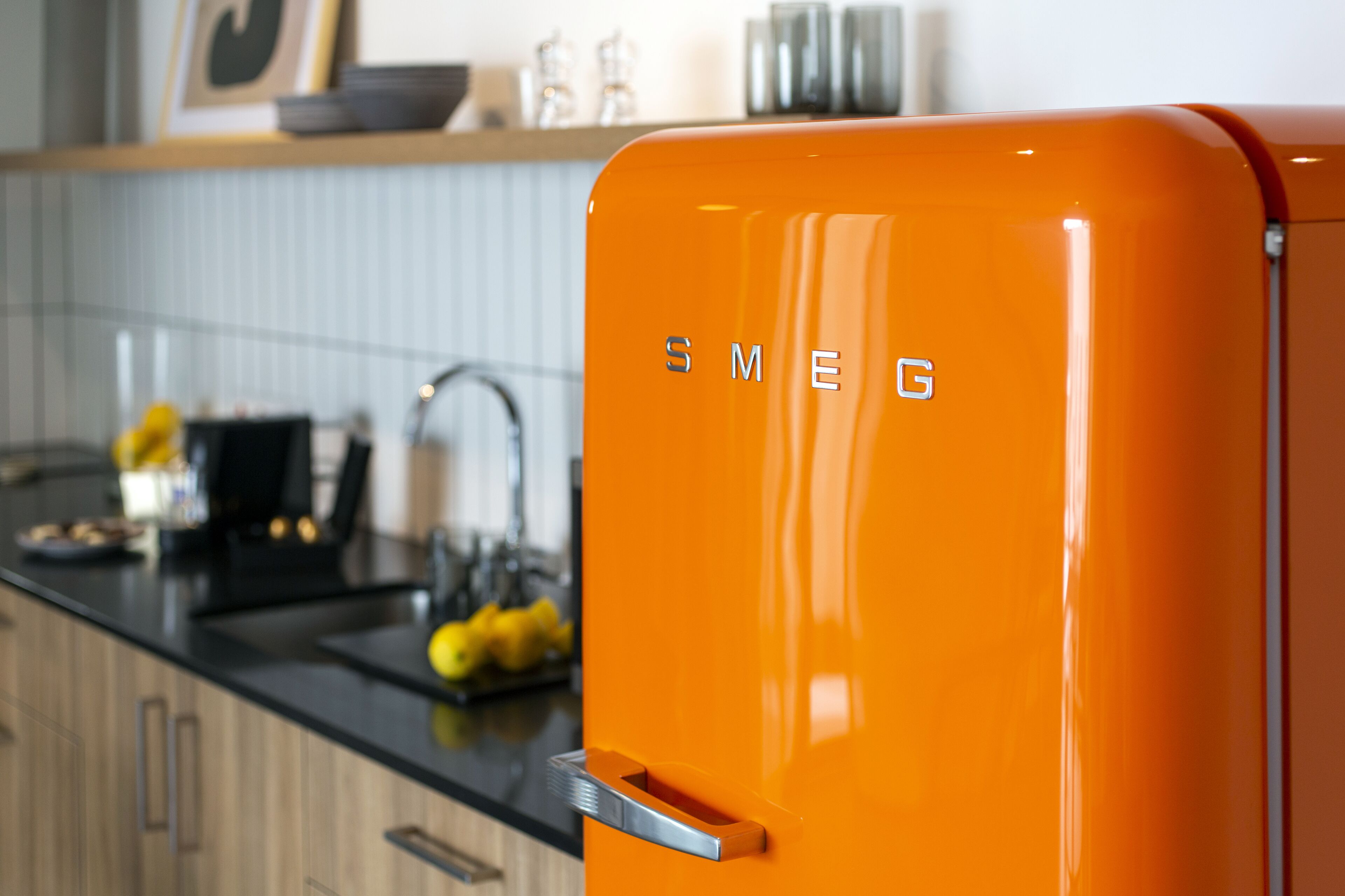 A kitchen with a bright orange refrigerator, wooden cabinets, and a black countertop.
