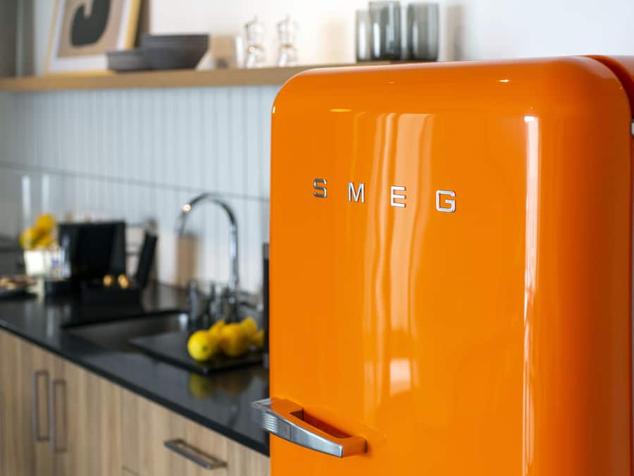 A kitchen with a bright orange refrigerator, wooden cabinets, and a black countertop.