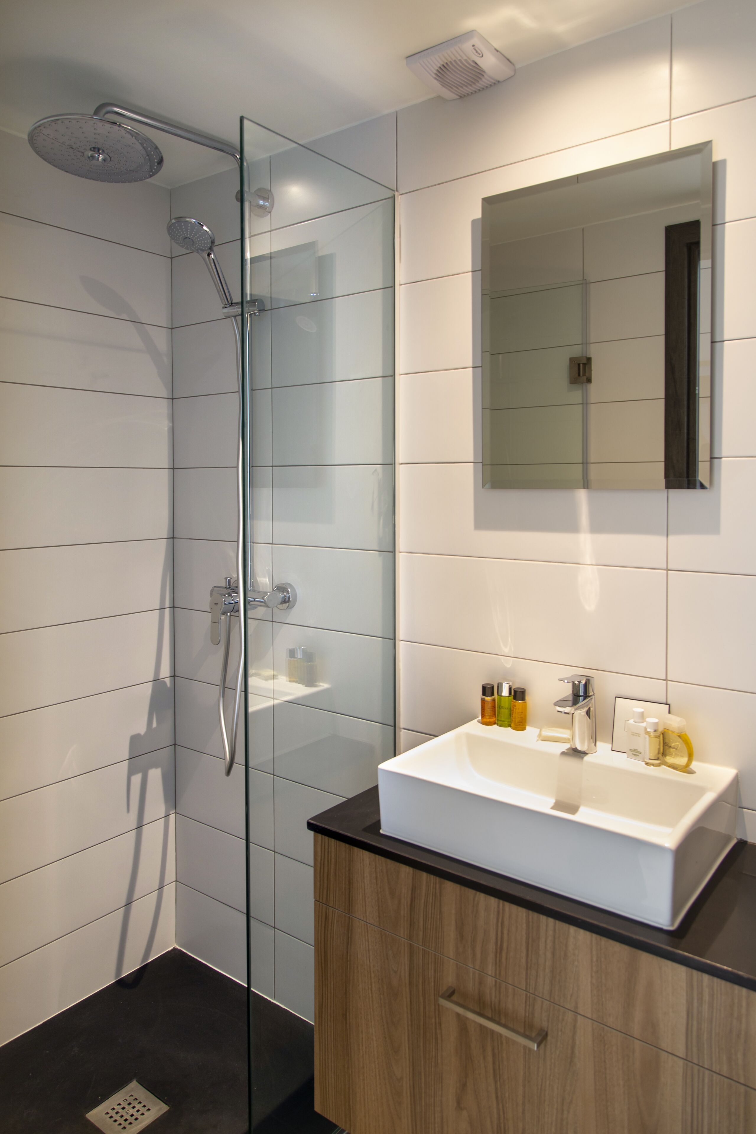 A modern bathroom with a glass-enclosed shower, a white sink with a mirror above it, and wooden cabinets.