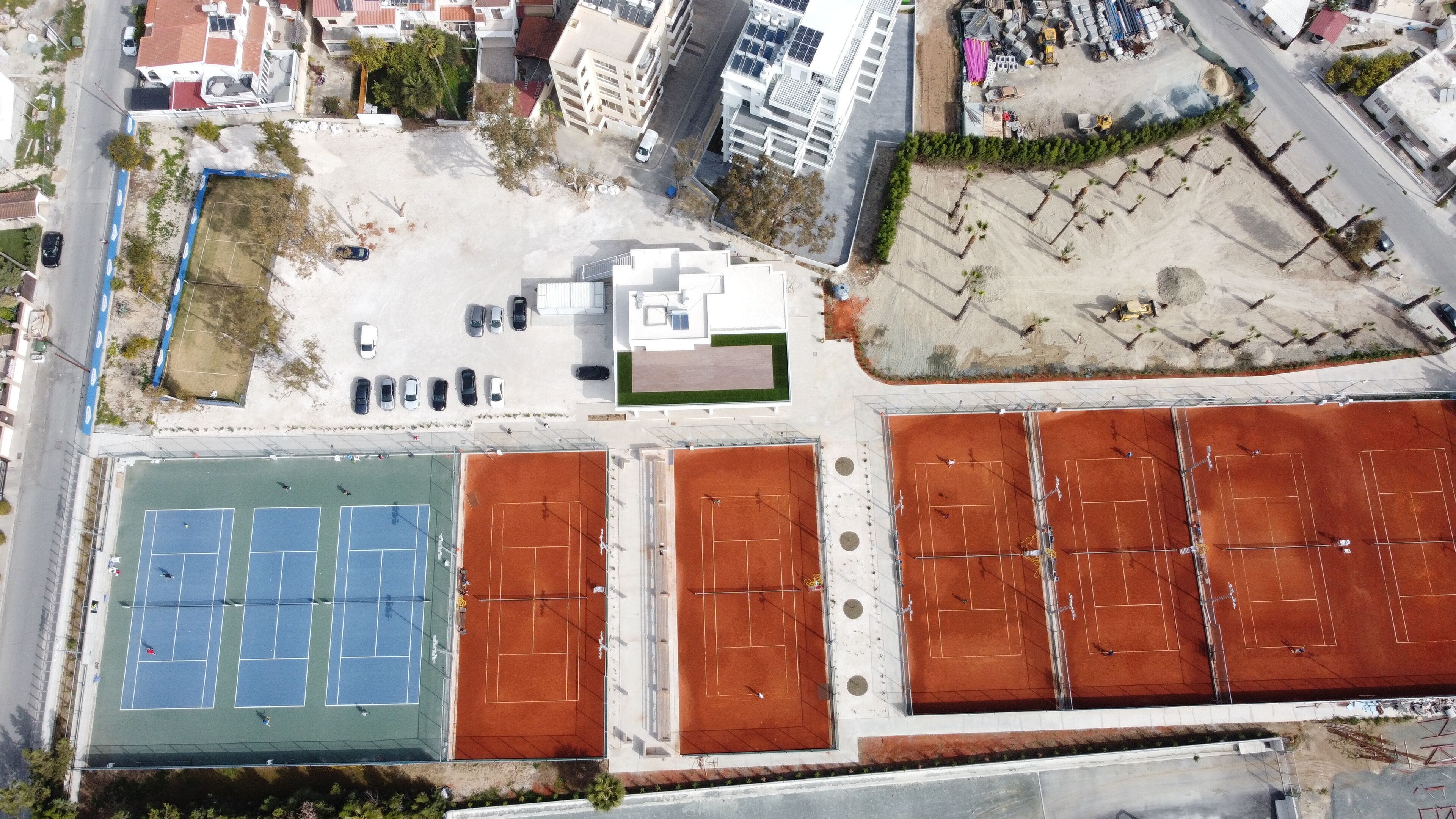 Vista aerea di un complesso sportivo con diverse piste da tennis, un'area parcheggio e edifici circostanti.