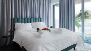 Quarto de hotel com uma cama grande, mesa de cabeceira, janela com cortinas e vista para o exterior.