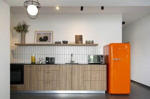 A modern kitchen with wooden cabinets, a black oven, a microwave, and an orange refrigerator.
