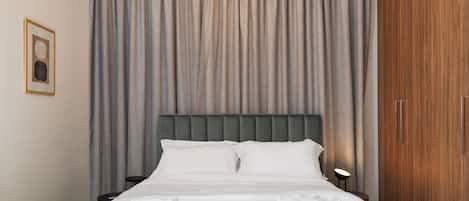 A neatly made bed with white linens and towels, a grey headboard, and a wooden wardrobe.