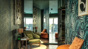 Uma sala de estar moderna com um sofá verde, um banquinho redondo laranja e uma parede com padrão.