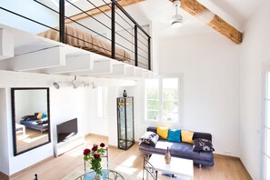 Uma sala de estar ampla com teto alto, escada, sofá com almofadas, televisão e um aparador de vidro.