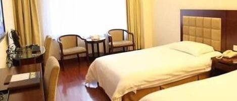 A hotel room with two single beds, a desk with a chair, a small table, and a lamp.