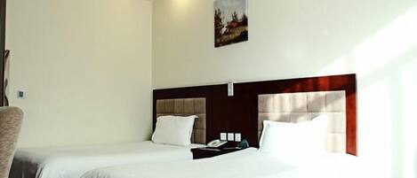 A hotel room with two beds, a wooden headboard, a painting on the wall, and a chair.