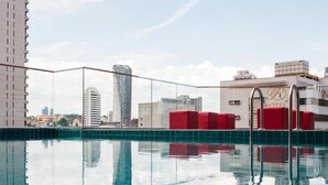Een dakzwembad met heldere weerspiegelingen van omliggende gebouwen, waaronder een hotel met een zichtbaar bord.