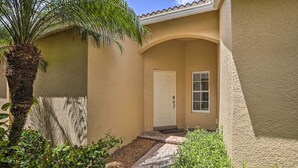 A house with a beige exterior, a white door, and a small porch area with a palm tree and plants. - Bright & Airy Fort Myers Home w/ Pool Access! (Fort Myers)