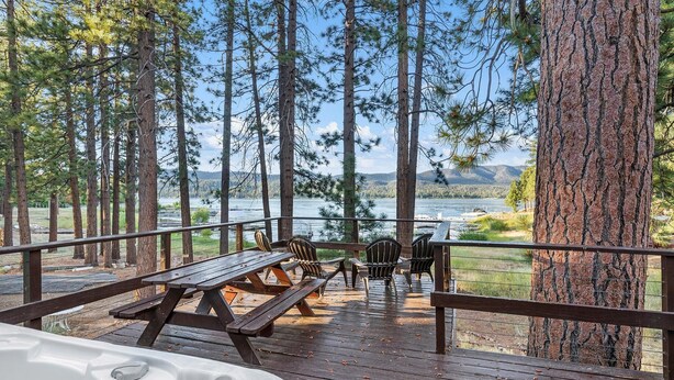 A wooden deck with picnic tables and chairs overlooking a lake, surrounded by tall trees.