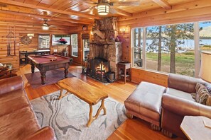 Un intérieur de chalet chaleureux avec une table de billard, des canapés en cuir, une cheminée et une vue sur un lac.