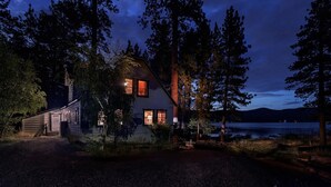 A cabin with a sloped roof, a visible chimney, and a window with a curtain.