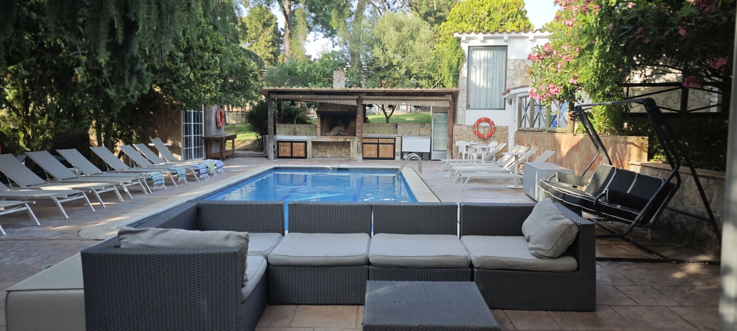Un área de piscina con sillones de descanso, una barbacoa integrada y una chimenea de piedra.