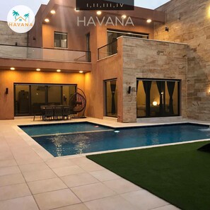 Una villa moderna con piscina, mobiliario exterior y fachada de piedra.