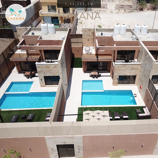Un moderno edificio residencial con dos piscinas, mobiliario exterior y depósitos de agua en el techo.