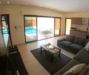 A spacious living area with a sofa, a coffee table, and a view of a pool through a sliding glass door. - Havana Villa-Luxurious stay in Dead Sea\Al-Ghour (Juwafat al-Kafrayn)