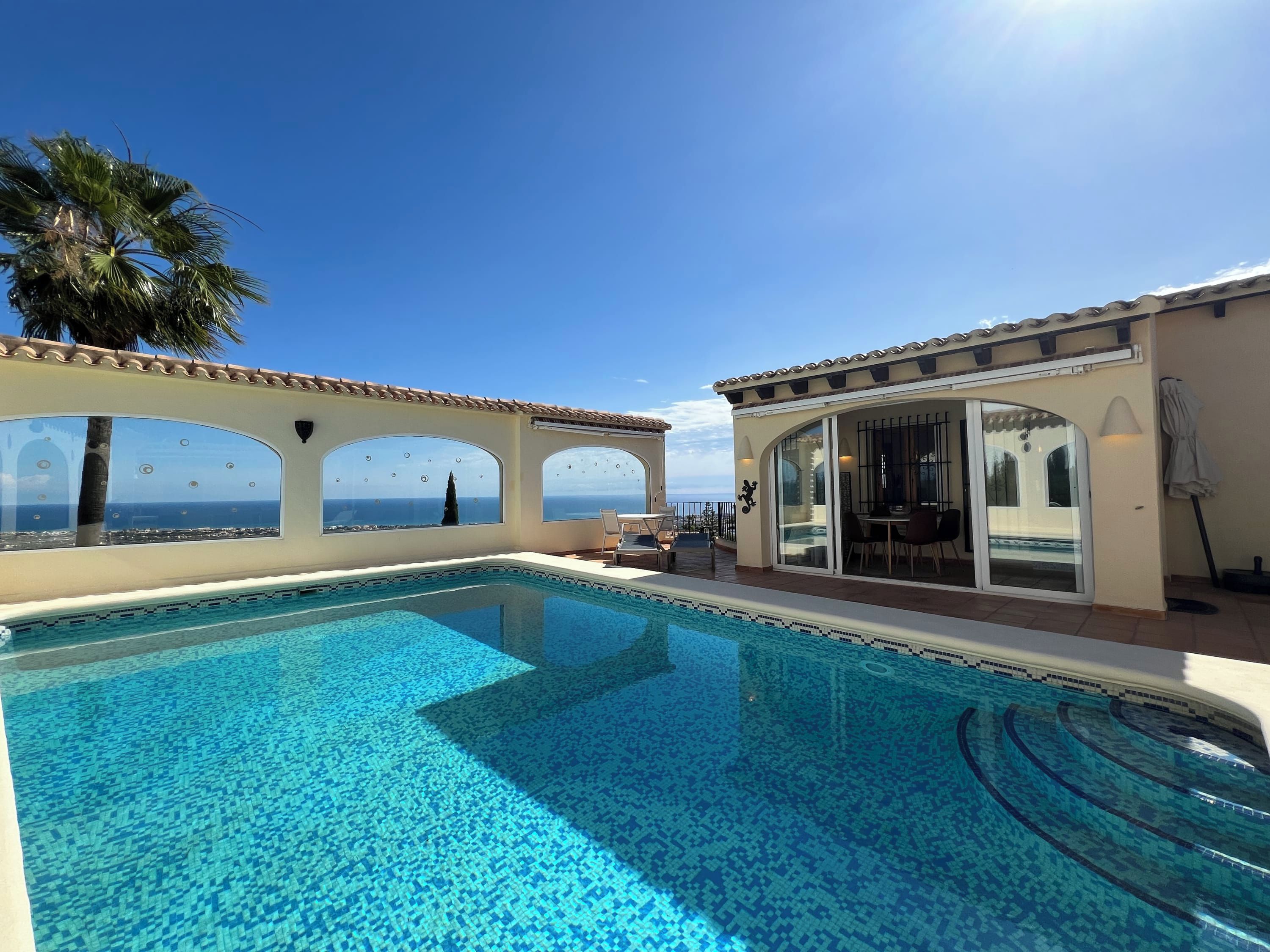 Ein Poolbereich mit freiem Blick auf das Meer, eine überdachte Lounge-Ecke und ein gefliester Pool.