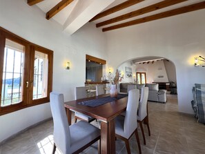Ein Essbereich mit Holztisch und Stühlen, eine Küche im Hintergrund und ein Blick durch ein Fenster.