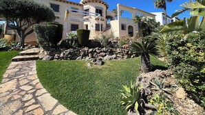 A well-maintained garden with a stone pathway leading to a building with multiple balconies and a clear blue sky. - T-0121, Canarios, Fantastic villa with panoramic sea views (Denia)
